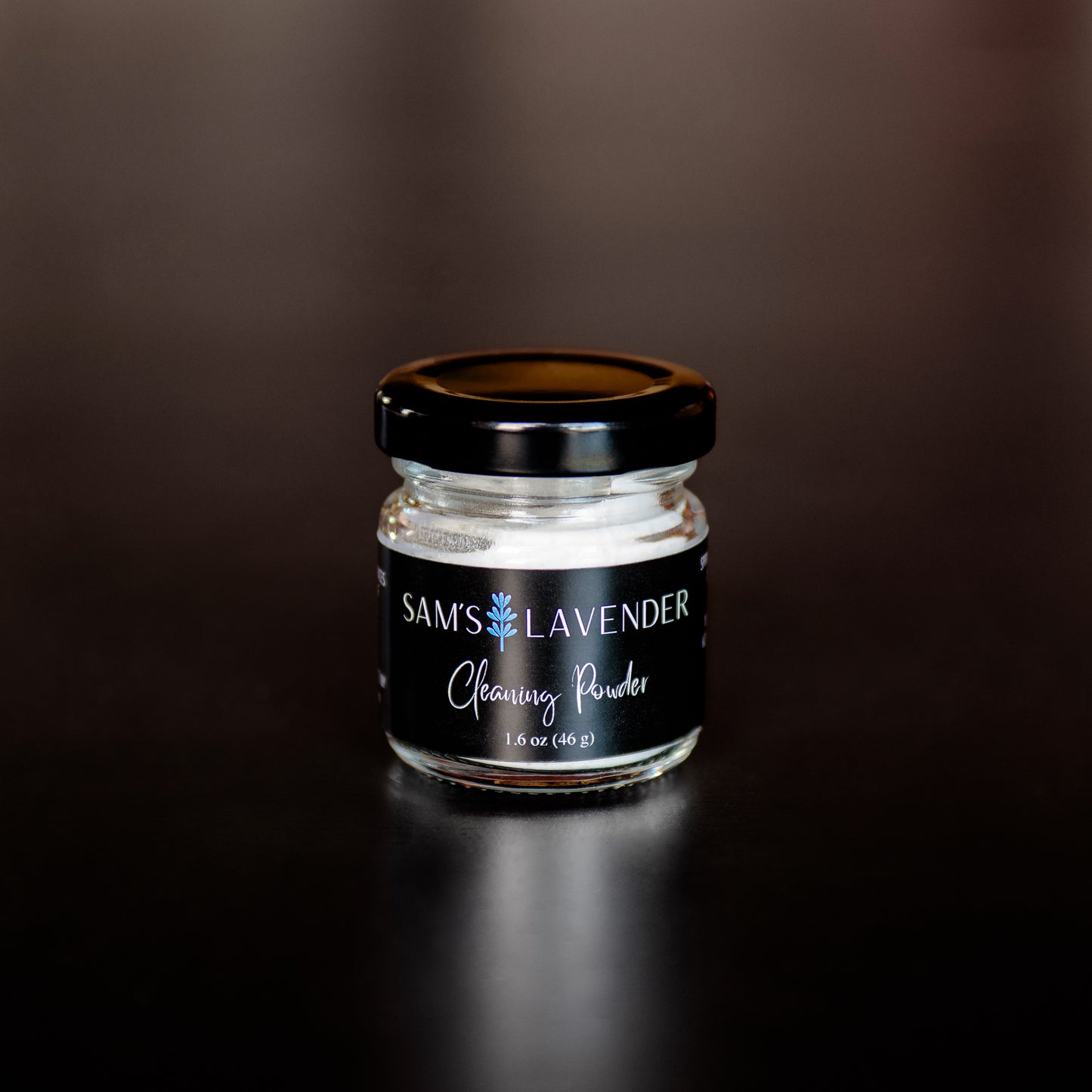 A small clear glass jar with a black lid labeled "Sam's Lavender Cleaning Powder"