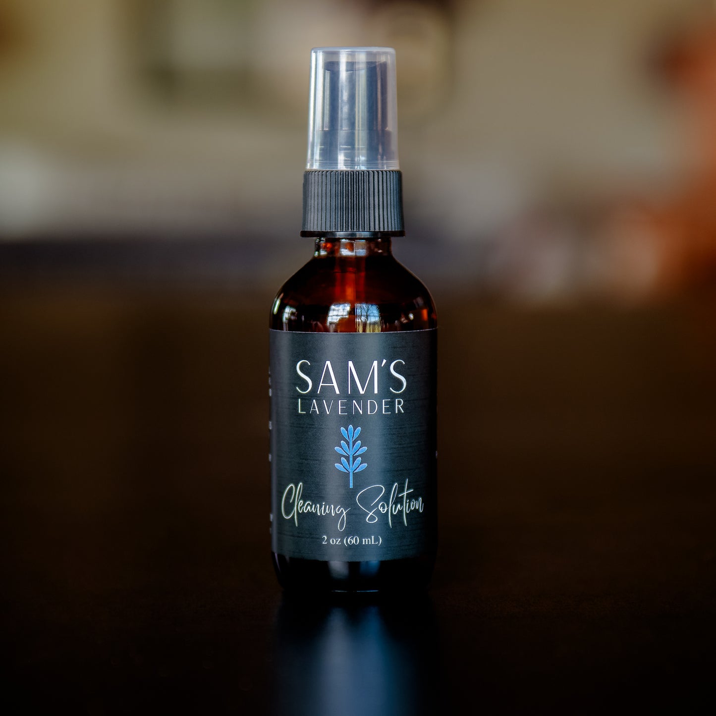 An amber glass spray bottle labeled 'Sam's Lavender' with a black spray nozzle, on a wooden surface with a blurred background.
