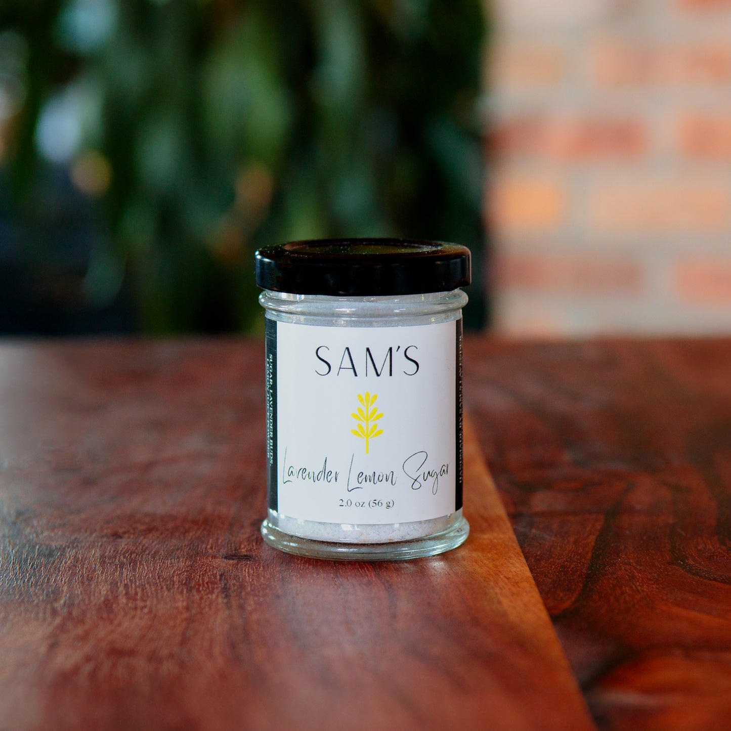 A glass jar of Sam's Lavender Lemon Sugar placed on a wooden surface with a blurred background.
