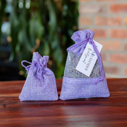 Two lavender sachets tied with purple ribbons, one small and one large, with a tag on the larger one displaying the brand name.