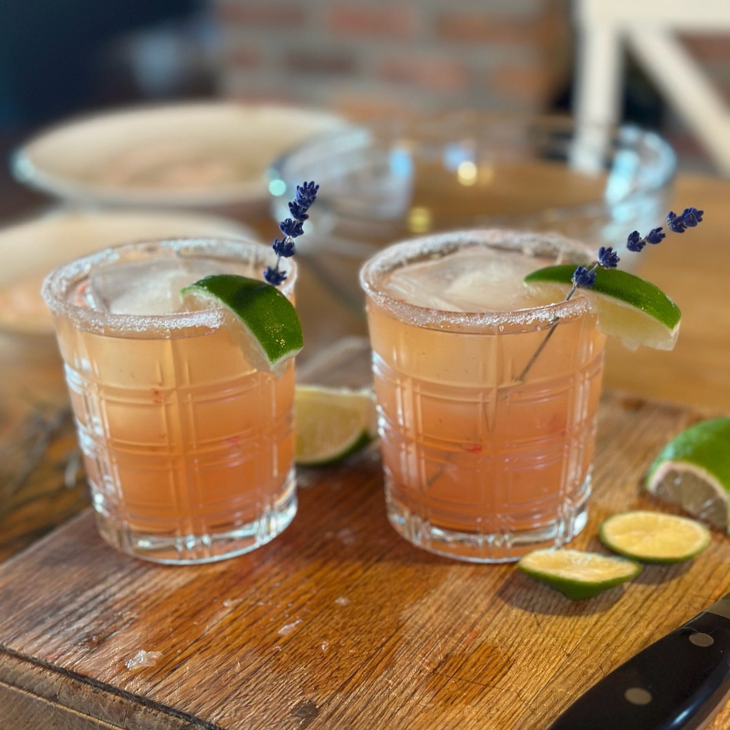 Two rocks cocktail glasses with a sugar rim, lime, and lavender cocktail stick garnish.
