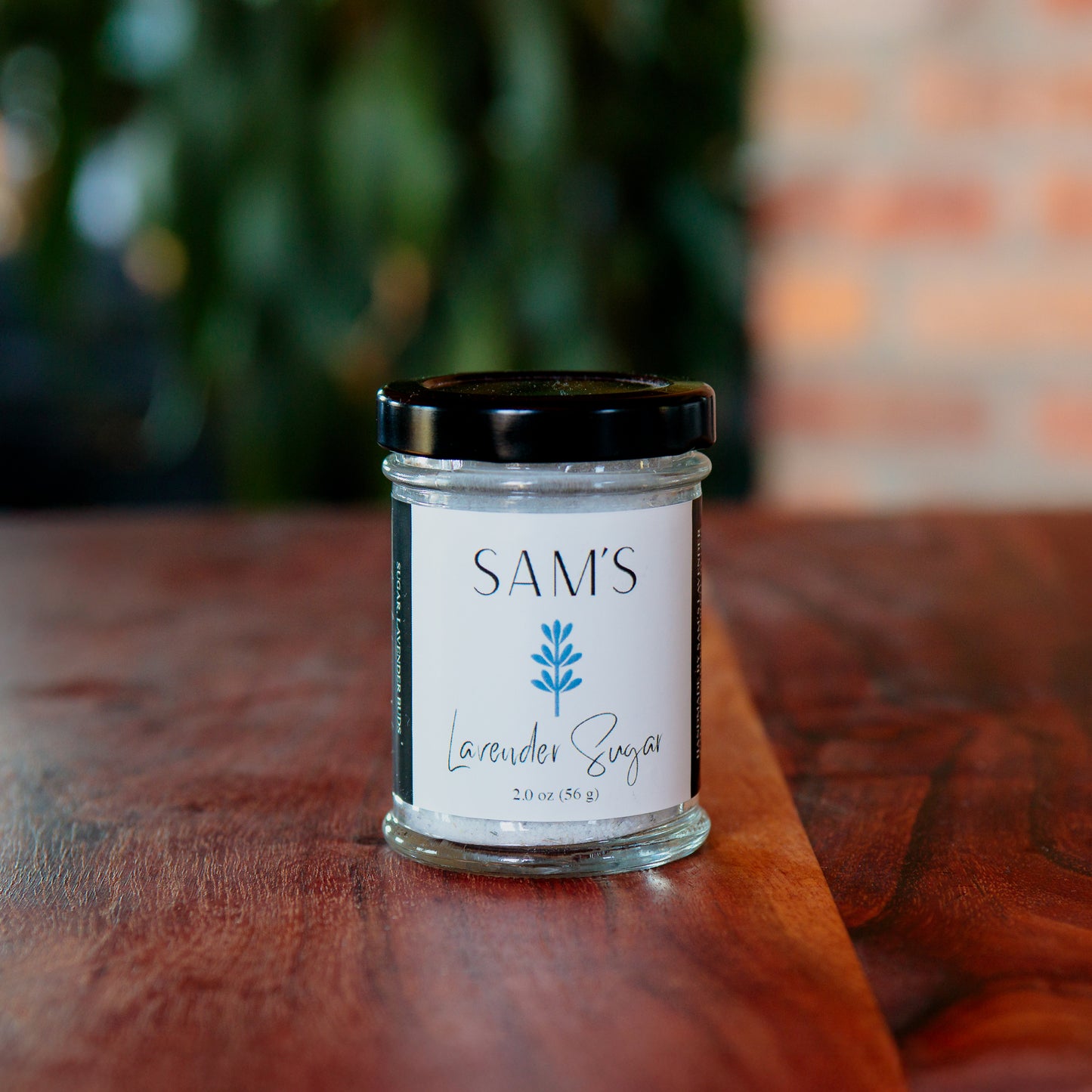 A glass jar labeled 'Sam's Lavender Sugar 2oz' containing lavender sugar, placed on a wooden surface.