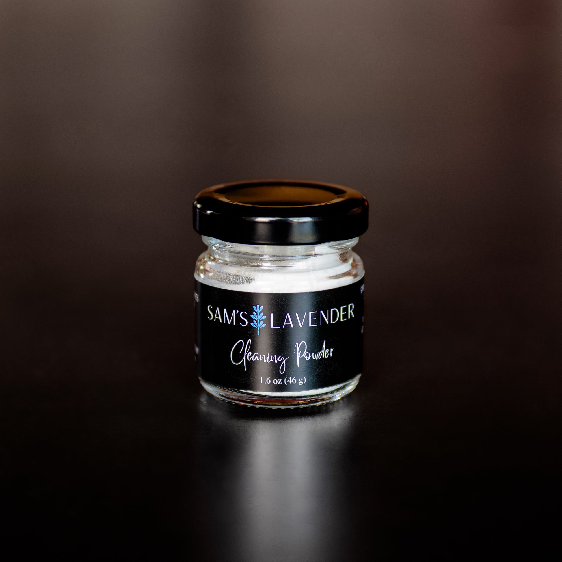 A small clear glass jar with a black lid  labeled "Sam's Lavender Cleaning Powder" 