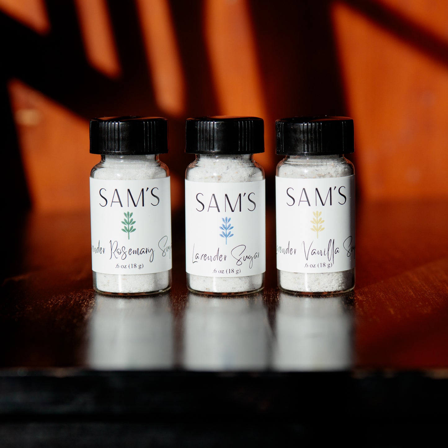 Three glass vials with lavender sugar, lavender rosemary sugar, and lavender vanilla sugar, all with a black cap
